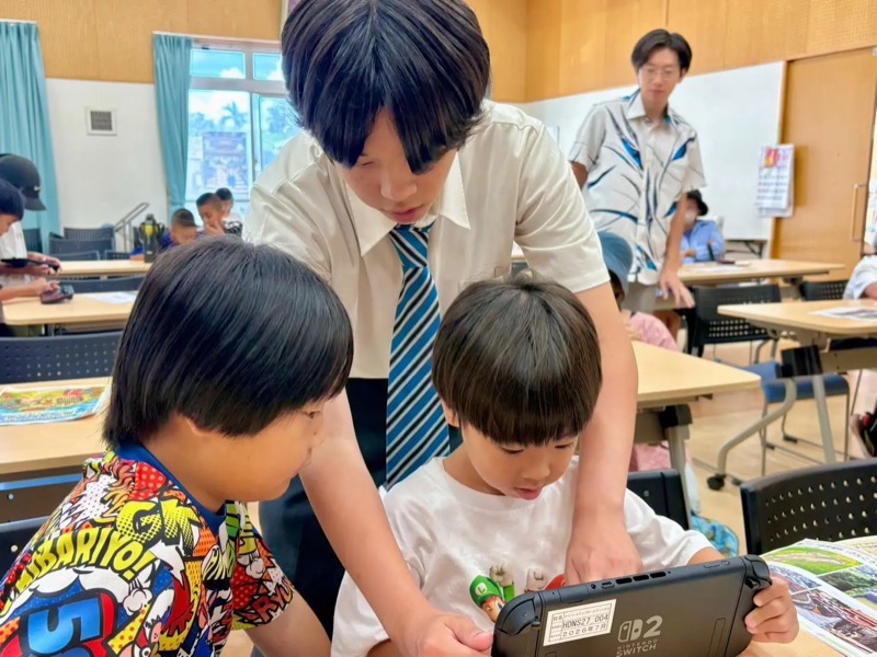 越来自治公民館で高校生ボランティアと子どもたちがタブレットを囲む様子