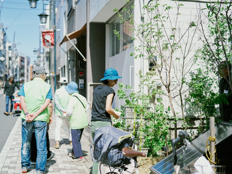 街中の小さな緑地に立ち寄り植物を眺める地域の人々